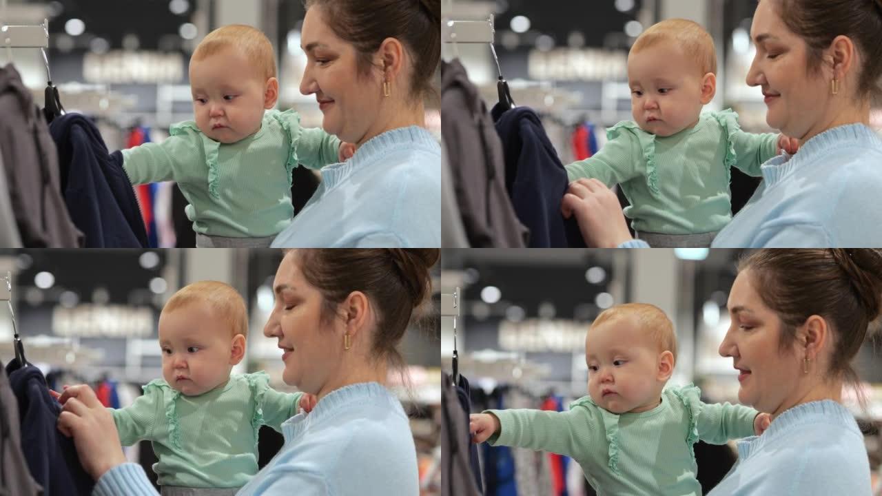 逗乐的女婴想在商店里和妈妈一起买衣服