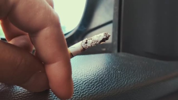 司机在车里抽烟。在汽车敞开的窗户上，一个人把手放在里面，烟在里面。特写