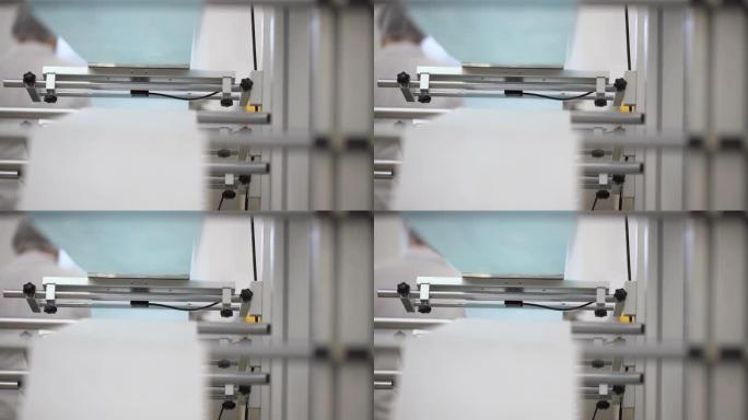 在工厂中，白色和蓝色棉纤维合并成医用口罩的特写镜头。制造呼吸医用口罩的自动化机械。
