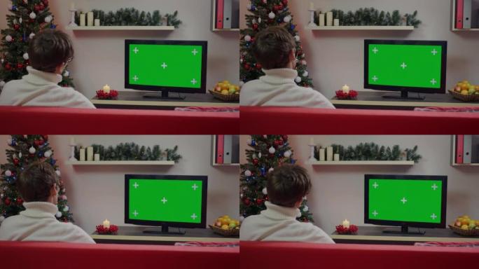 一个男人在圣诞节装饰的客厅里看绿屏模型电视。