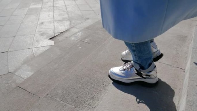 穿着白色运动鞋的无法辨认的女性腿从楼梯上走下来。在大城市散步
