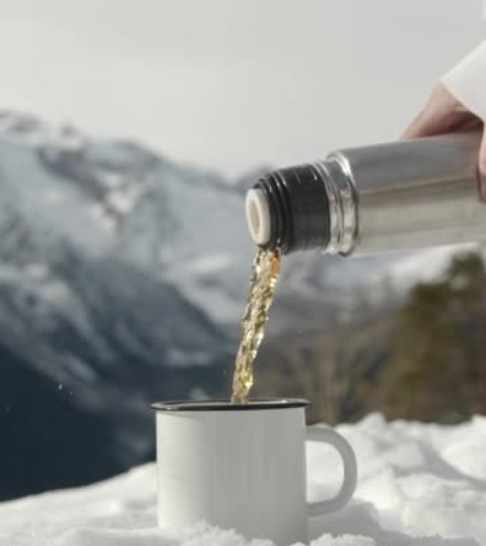人们将热水瓶中的新鲜热茶倒入雪中雪中的杯子中。