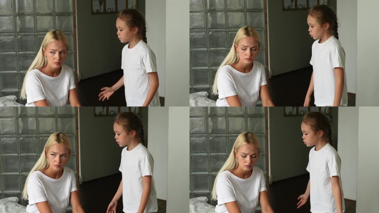站在愤怒的小孩女儿的肖像责骂，提高声音，尖叫着悲伤的年轻母亲坐在家里的沙发上。