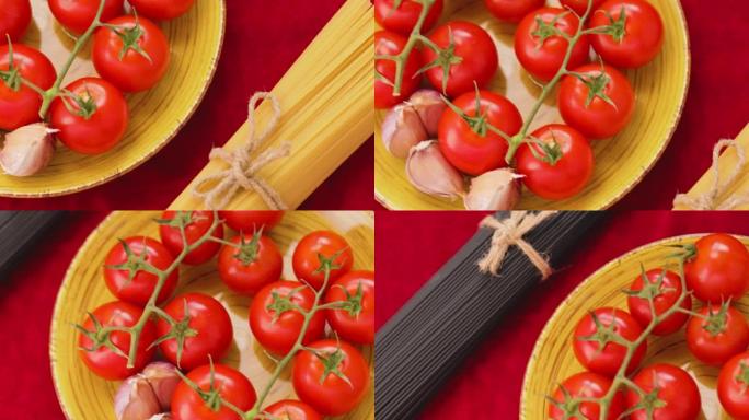 黑色和黄色意大利面，西红柿和大蒜放在红色织物上。黄色盘子上的新鲜蔬菜和两束麻线意大利面。顶视图。手持