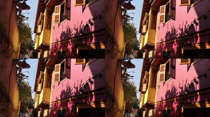 在土耳其安塔利亚老城区，一只小乌龟鸽子在粉红色墙壁和木制百叶窗的老房子之间飞翔。视频9秒