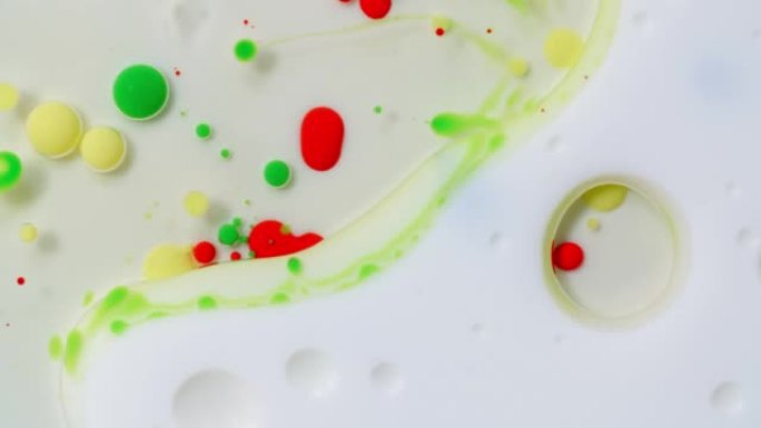 彩色丙烯酸涂料气泡散布在白色表面上，并混合在抽象的纹理和设计中。红色、绿色和黄色油墨球滴和混合。奇妙