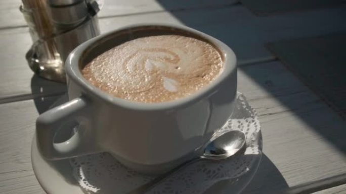 夏季咖啡馆桌上的一杯卡布奇诺咖啡，阳光和坚硬的阴影