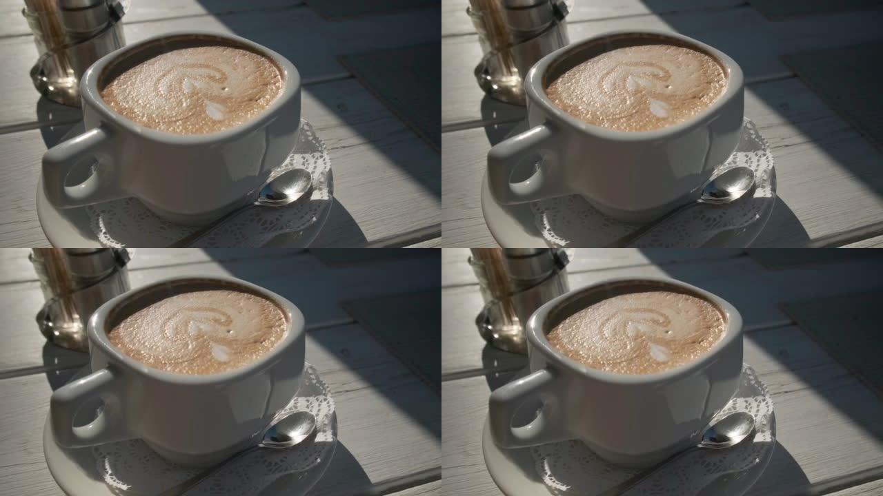 夏季咖啡馆桌上的一杯卡布奇诺咖啡，阳光和坚硬的阴影