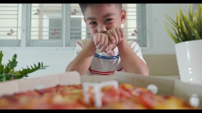 快乐的亚洲小男孩5年打开披萨纸板，在家里的桌子上非常惊讶和快乐