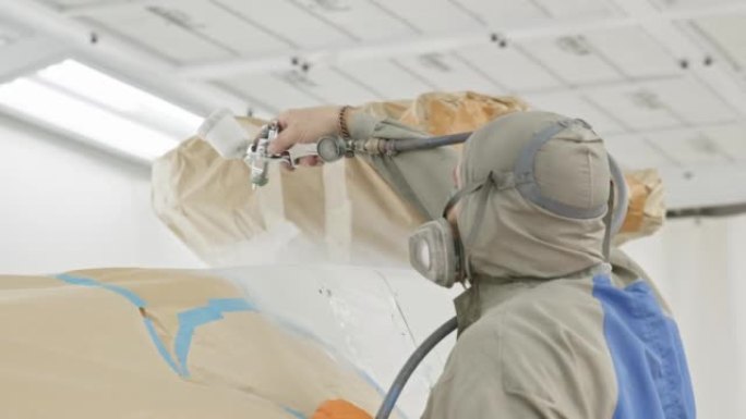 画家手中的喷漆室喷枪的近景。工人油漆直升机或汽车的顶部。白色油漆以慢动作近距离喷涂。工人恢复飞机。