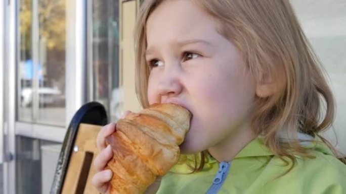 一个可爱的欧洲女孩在户外的长椅上咬一口大羊角面包，咀嚼食欲很好。青少年在甜食甜点上吃零食，里面有巧克