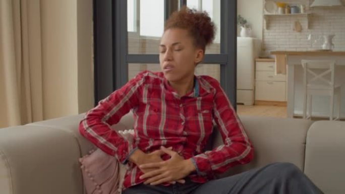 沙发上患有腹痛的不舒服的黑人女性