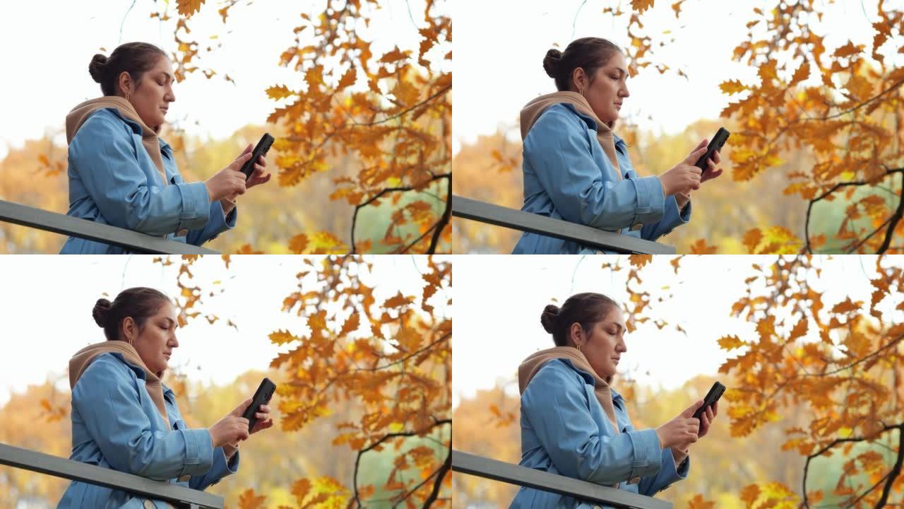 女人站在秋天公园的阳台上看电话