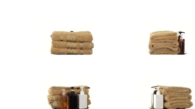 一叠几条浴巾，用于水疗的毛圈，在白色背景上旋转。毛巾和带有沐浴露和洗发水的瓶子。水疗用品。