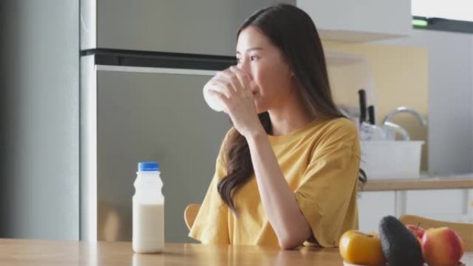 年轻的亚洲妇女在家中厨房喝牛奶，健康的生活方式