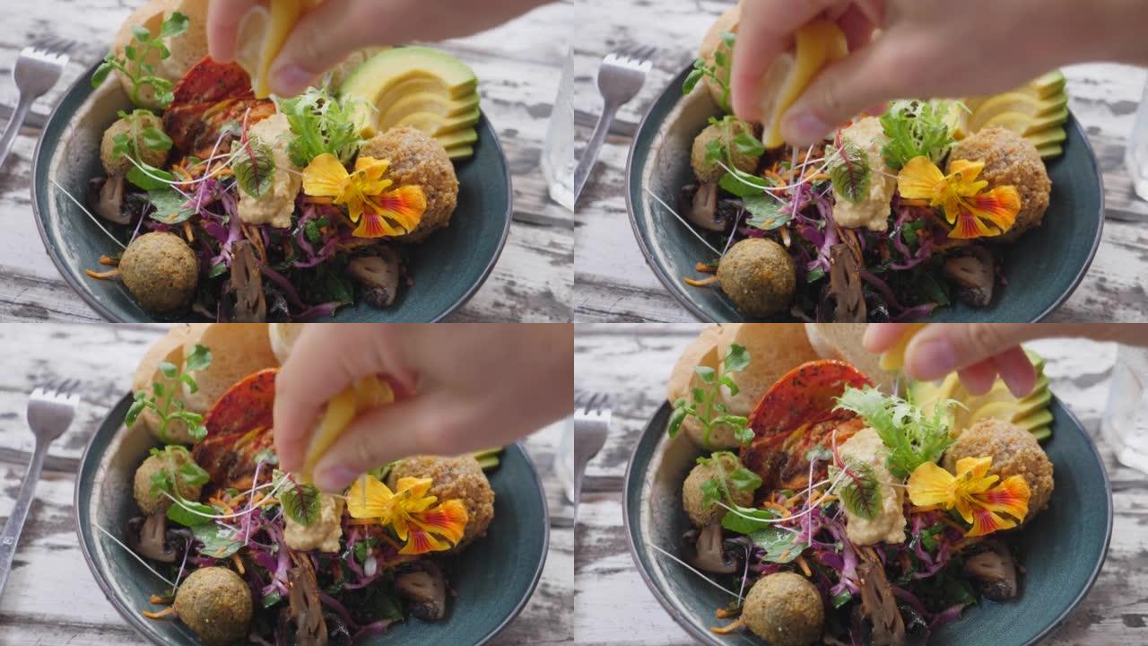 一只手的俯视图，手指挤压一片柠檬，从其中挤出果汁，然后将其溅到佛陀碗中的健康美味的纯素食食品上。健康