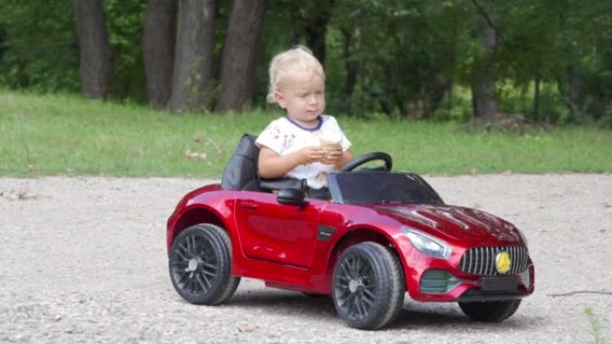 快乐的孩子吃冰淇淋在夏季公园驾驶电动玩具车。1.5岁的小孩玩得开心骑电池动力汽车。小男孩骑着小汽车玩