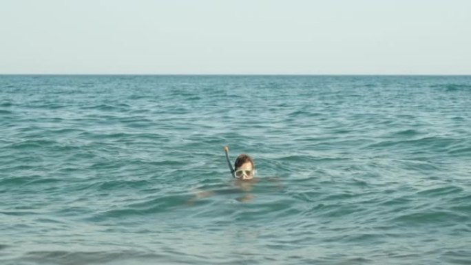 一个戴着潜水面具的男人在海浪上摇摆，只有他的头在表面上可见。看着摄像机。