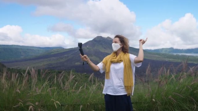 在新型冠状病毒肺炎大流行期间，一名戴着口罩的旅游博客作者在山里用相机拍摄自己。她向追随者展示了如何在