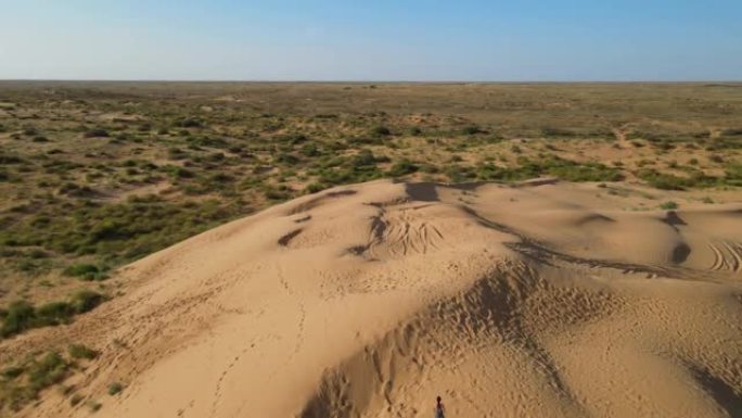 无人机的鸟瞰图。夏天，在阿斯特拉罕 (Astrakhan)，穿着长豹子连衣裙的女人沿着沙漠中的高沙丘