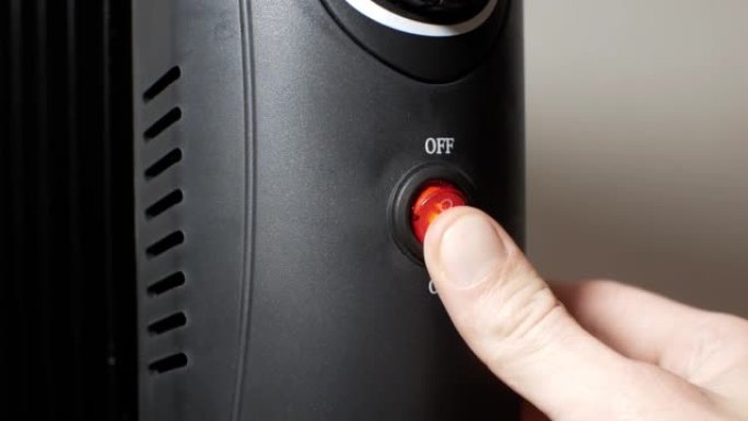 男人在家里按下电暖油电热散热器的电源按钮。“开” 或 “关” 调谐模式。家庭供暖和保温的概念。黑色充