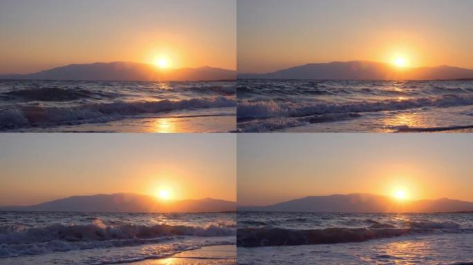 平静的海面上令人惊叹的美丽日出。黄色的太阳升起在海洋和山脉之上，太阳路径在水上。阳光和太阳光线反射在