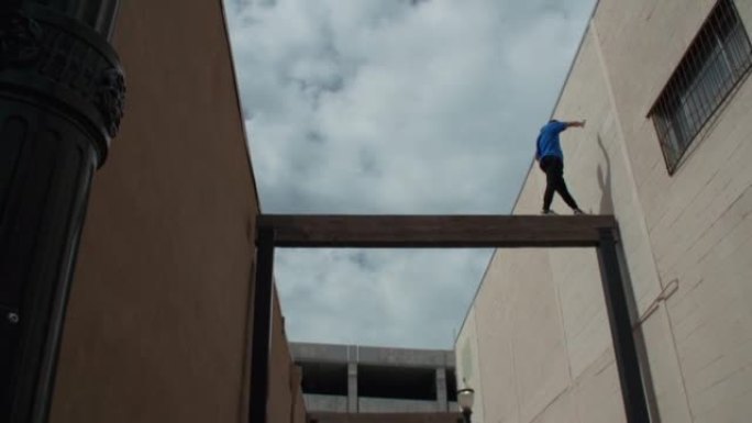 一名年轻男性在建筑物之间的杆子上做跑酷的低角度镜头