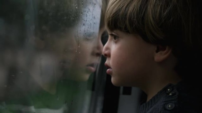 忧郁的小男孩靠在火车窗上，看着雨天经过的风景。小孩旅行