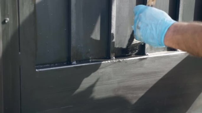 旧侵蚀门外的改造过程中，男工人在一次性防护手套上涂刷门表面，去除腐蚀纹理后最终呈黑色。侵蚀浇口的修复
