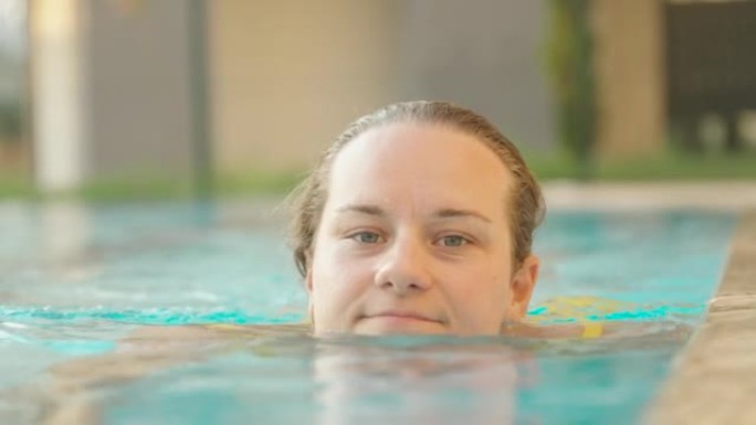游泳池里的一个女孩在相机的边缘游泳，看着它，然后游过，面对特写镜头，慢动作