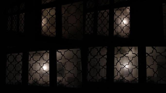 通过关闭的玻璃门在门上的未知阴影人物的轮廓。夜晚窗前的人的剪影。可怕的场景万圣节概念的模糊剪影的疯子