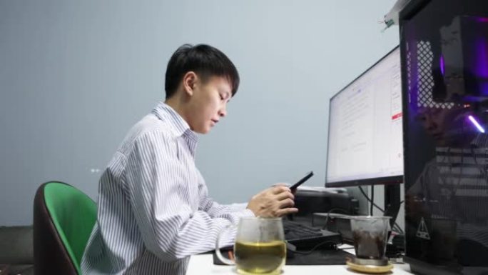 晚上，一名亚裔男子在电脑前拍照发送信息，报告工作进展 -- 年轻人的生活方式