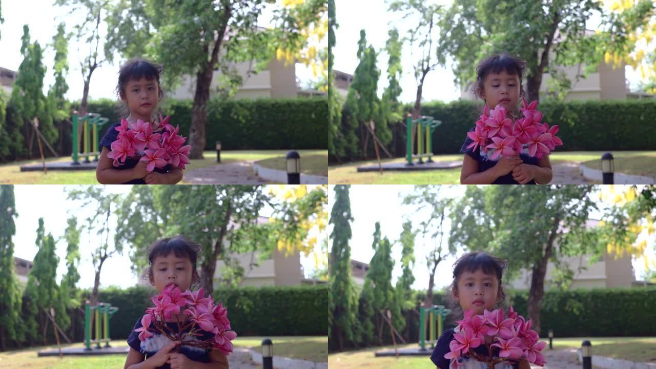 一个亚洲小女孩拿着粉红色的花朵向镜头展示的慢动作镜头