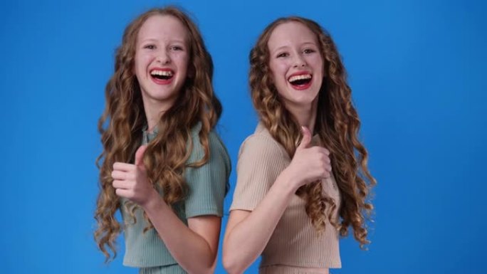 两个双胞胎女孩的4k视频在蓝色上竖起大拇指。