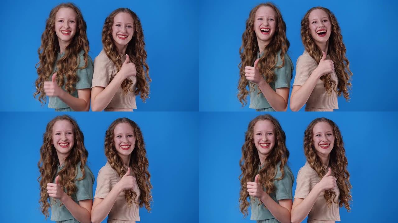 两个双胞胎女孩的4k视频在蓝色上竖起大拇指。