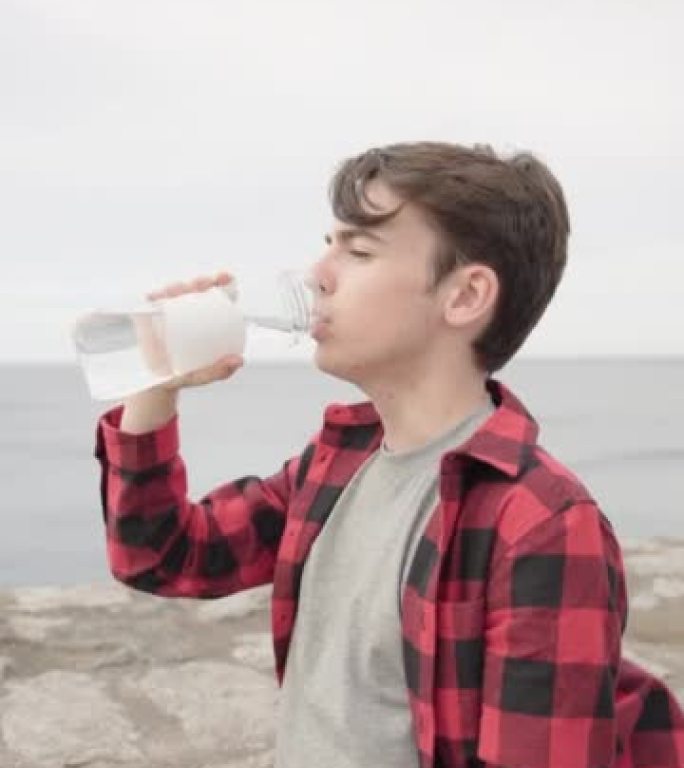 英俊的少年男孩在户外用瓶子喝水。