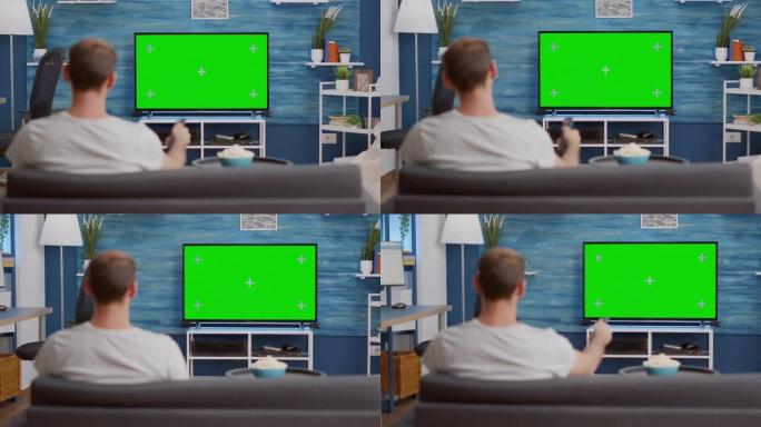 男人看着电视上的绿屏，坐在现代客厅的沙发上切换频道