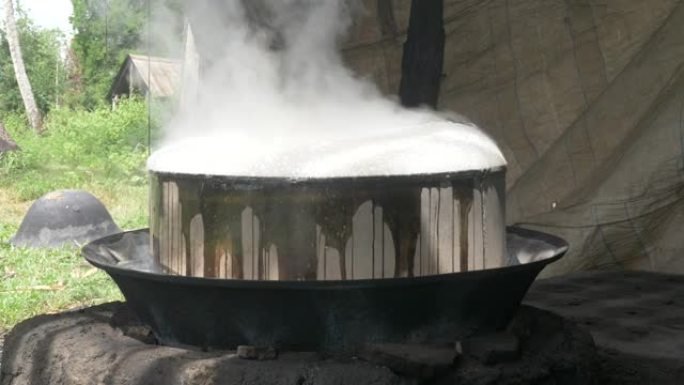 高棉传统糖棕榈制造商。在露天燃烧的木头上关闭炒锅。棕榈糖在里面煮。