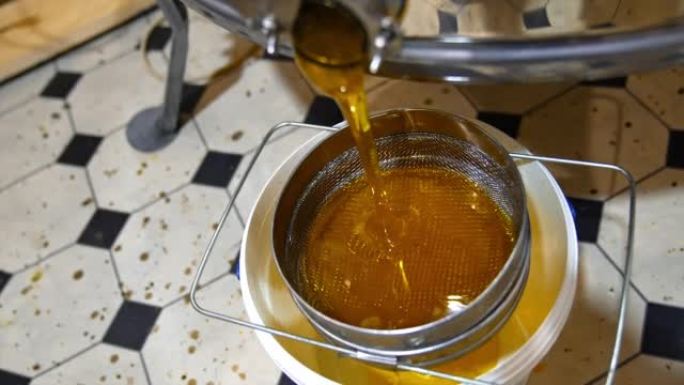 抽水后从蜂蜜提取机水龙头泄漏的新鲜蜂蜜。液体有机产品在筛子上流动。顶视图。