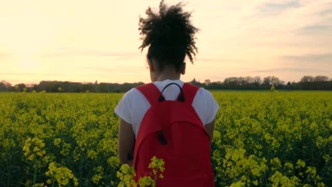 非裔美国人混血儿女孩青少年女年轻摄影师与红色背包和相机在黄色花田拍照