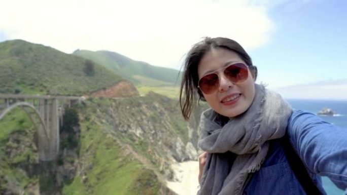 年轻女孩游客在明亮美丽的日子里通过视频电话交谈，分享大苏尔景观和岩石海岸线。戴墨镜的旅行者女人脸部摄