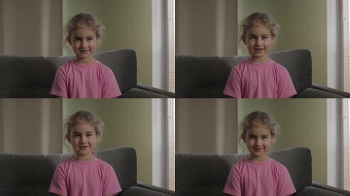 儿童女孩在线视频通话录制坐在沙发上，肖像。看着相机微笑的有趣女孩。快乐可爱的小视频记录器打你好，看着