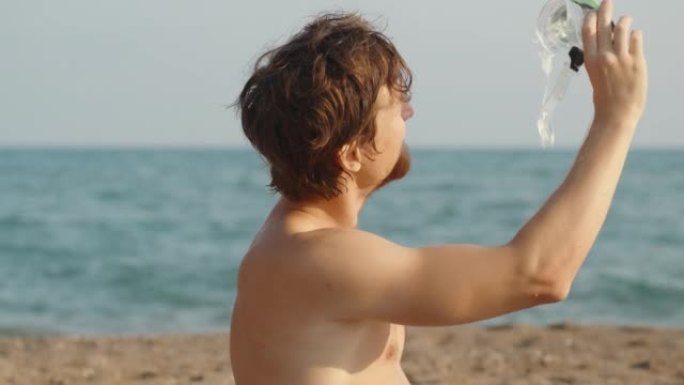 海滩上留着红色胡须的男人拿着水肺护目镜，看着太阳。大海在背景中。慢mo