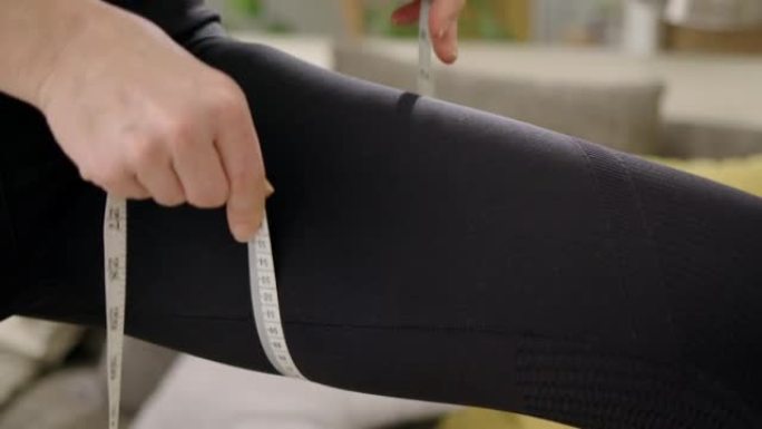 运动女孩用卷尺测量她的身体。穿着运动服的苗条女人测量她的大腿。减肥或肥胖的概念，健康的生活方式，在家