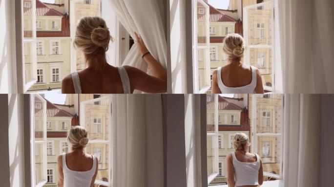 快乐的年轻女子打开窗帘，透过窗户往外看。