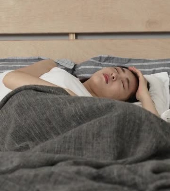 垂直屏幕: 亚洲日本女性躺在床上翻腾，由于家里现代卧室的床垫质量不好，感到不适。