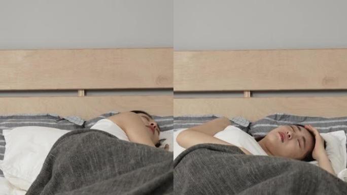 垂直屏幕: 亚洲日本女性躺在床上翻腾，由于家里现代卧室的床垫质量不好，感到不适。