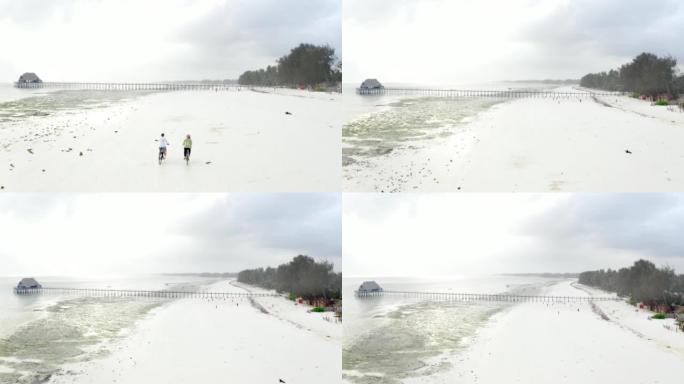 4k视频几个骑自行车的人沿着沙质Kiwengwa海滩行驶。放飞洛克家伙踢足球的镜头。健康的生活方式，