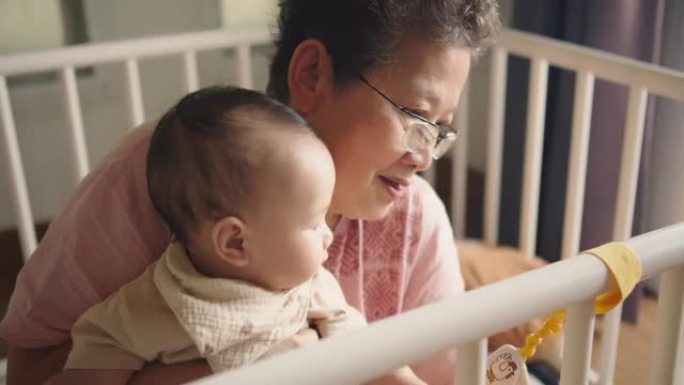 幸福的家庭开朗的亚洲高级女人祖母抱着和可爱的小婴儿蹒跚学步的孙女一起笑，一起拥抱爱，坐在家里的室内房