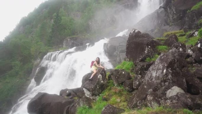 挪威山区瀑布附近的女人坐在岩石上，就像骑马一样